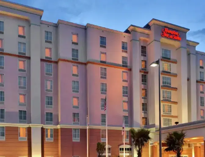 Exterior view of Hampton Inn & Suites Orlando International Airport Hotel featuring a multi story lit up building  displayed against a partly cloudy evening sky.