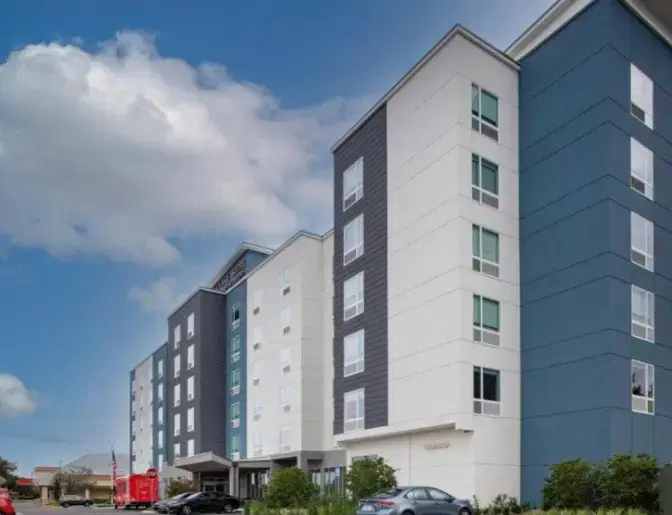 Exterior view of TownePlace Suites near Orlando Airport, showcasing a modern multi-story building with a blue and white facade under a partly cloudy sky.