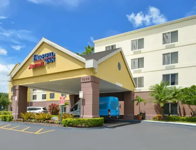 Exterior view of Fairfield Inn Orlando International Airport Hotel with a covered entrance, palm trees, and a blue van parked in front.