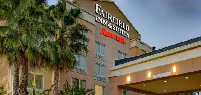 Exterior view of Fairfield Inn & Suites by Marriott Titusville, featuring a beige building with large windows, a covered entrance, and palm trees in the foreground.
