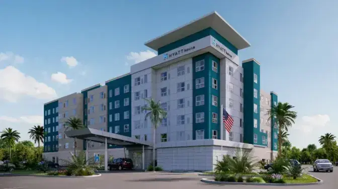 Exterior view of Hyatt House Hotel near Orlando International Airport, featuring a modern multi-story building with teal and white accents, a welcoming entrance, and palm trees under a clear blue sky.