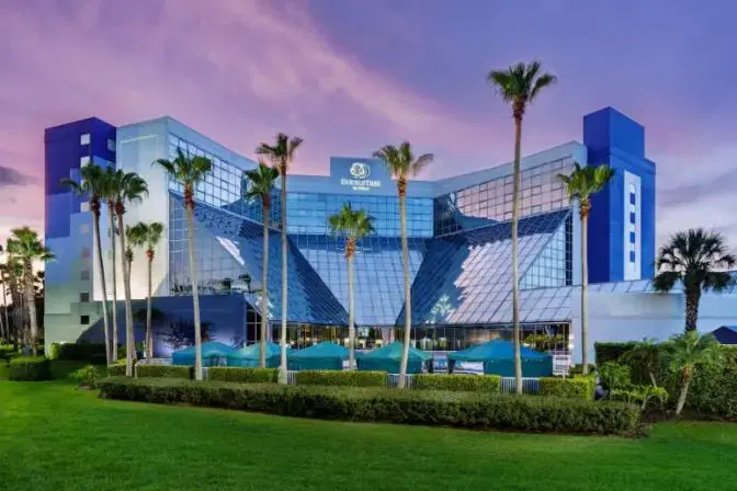 DoubleTree by Hilton near Orlando Airport, featuring a striking glass facade, palm trees, and a beautifully landscaped exterior at sunset.