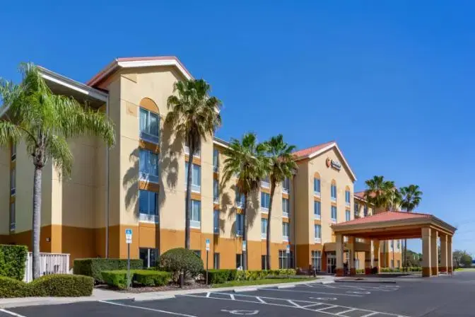 Exterior view of Comfort Inn & Suites Sanford hotel with a covered entrance, palm trees, and a well-maintained landscape under a clear blue sky.