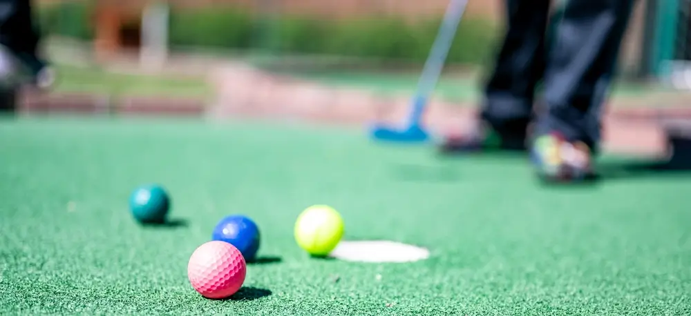 close up view of golf balls on miniature golf course with golfer and golf club in background
