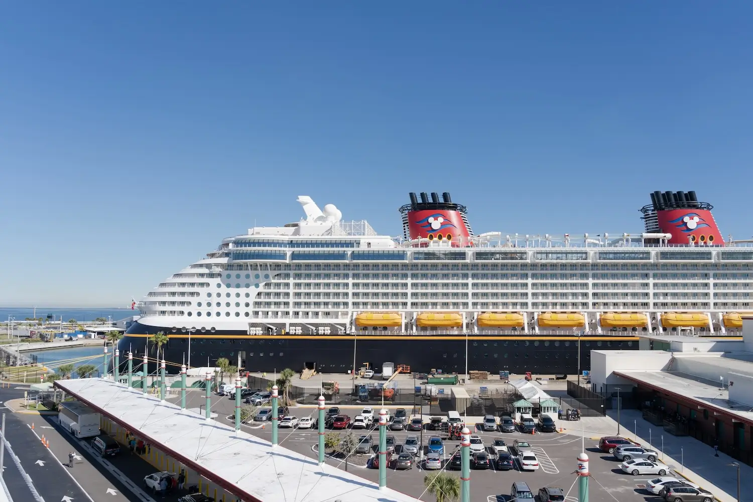 wide view showing disney cruise terminal entrance and parking lot at Port Canaveral in front of large disney cruise ship and blue sky