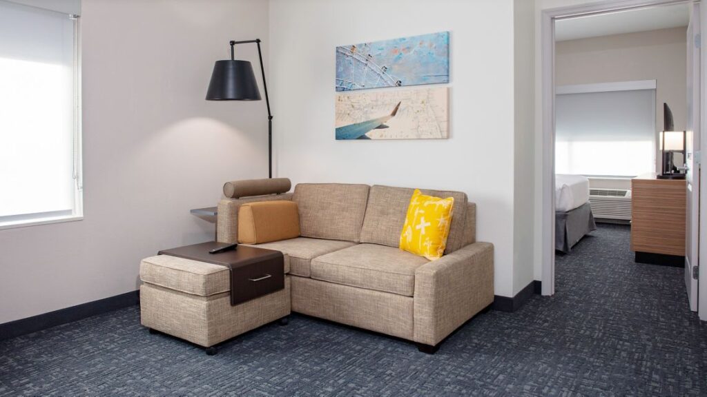 TownePlace Suites Orlando Airport hotel suite with tan couch and ottoman plus door to separate bedroom