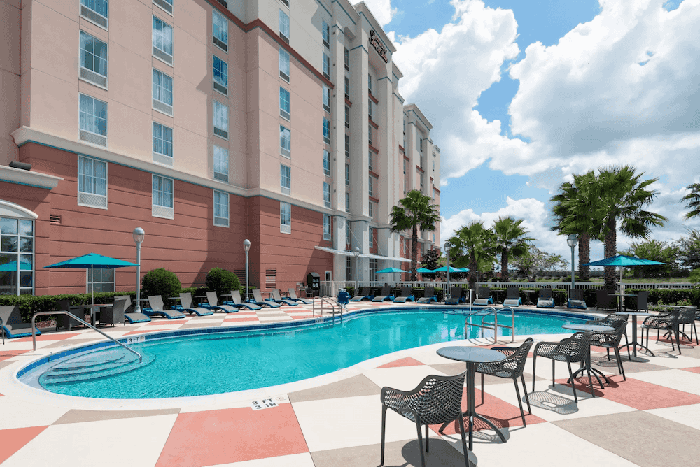 Outdoor pool and poolside chairs next to Hampton Inn and Suites Orlando Airport Gateway Village hotel
