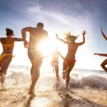 group of friends on beach running into the ocean