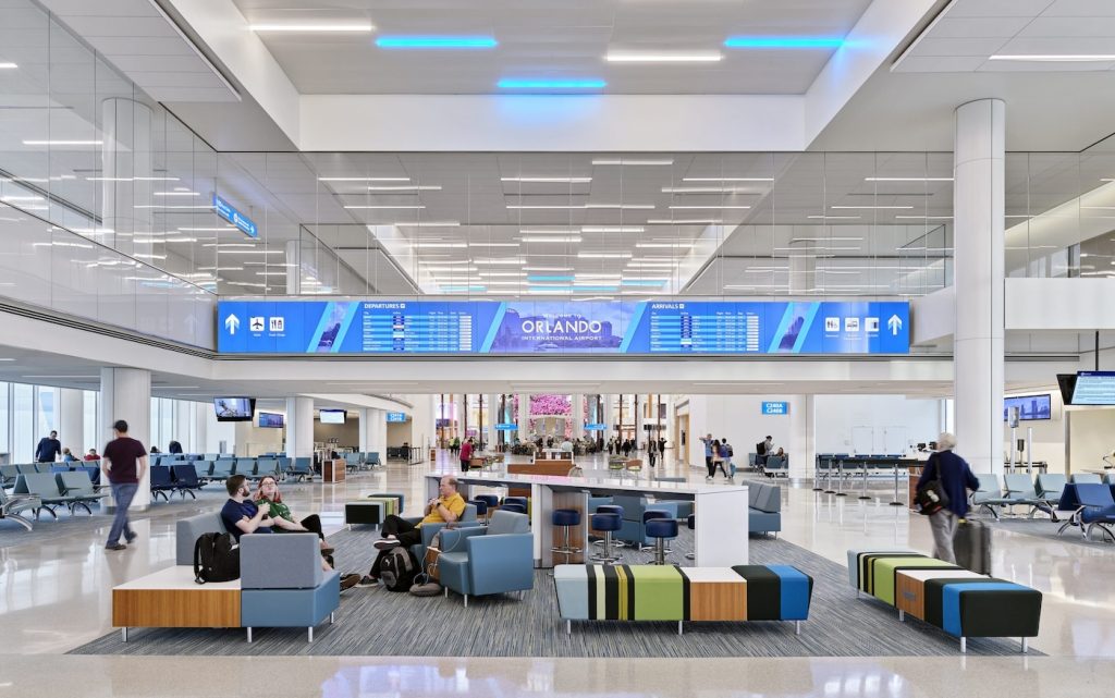 Interior view of terminal at Orlando International Airport showing chairs and a large screen with flight information and the word Orlando