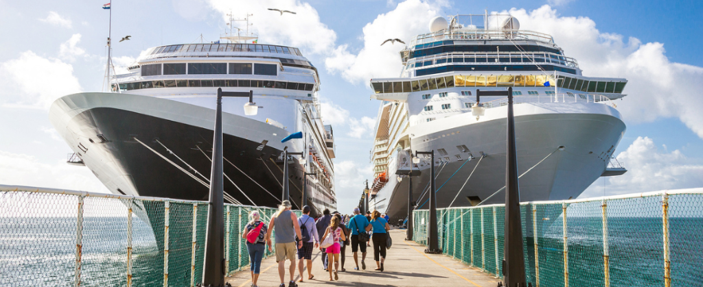 People walking on pier towards two cruise ships