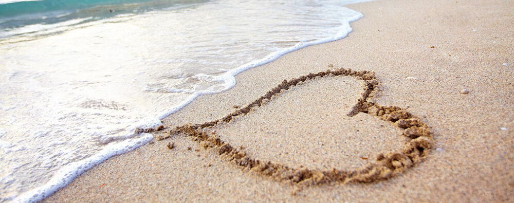 A heart shape drawn in the sand on a beach, which is gradually being washed away by incoming sea waves