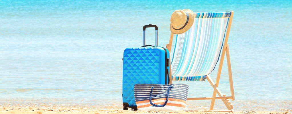 Packed suitcase, beach chair and accessories at sea shore. Vacation concept
