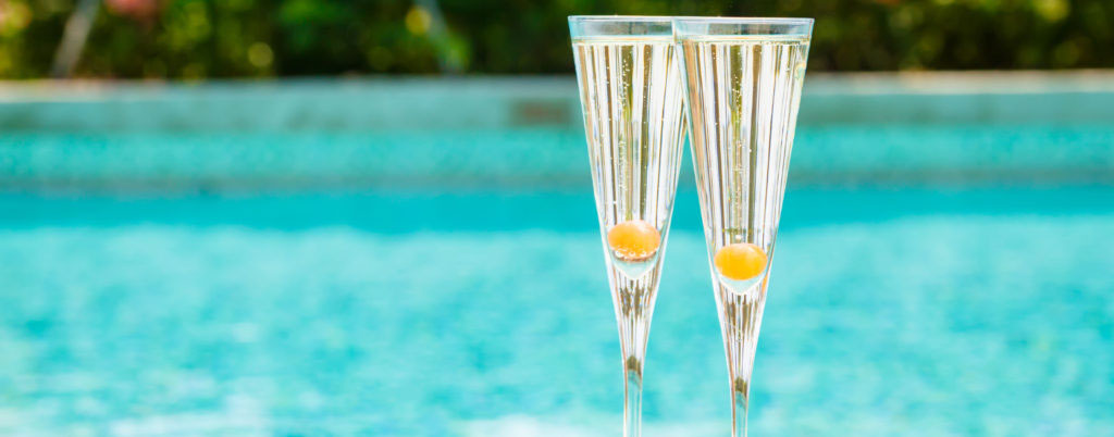 Two glasses of Prosecco cocktail with orange berry at the edge of a resort pool. Concept of luxury vacation. Outdoor pool background. Horizontal widescreen format