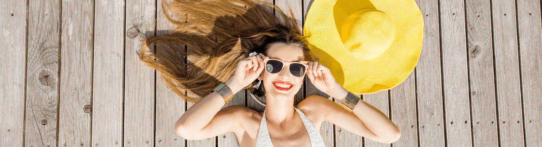 Young woman laying on a boat dock wearing sunglasses with a floppy sun hat
