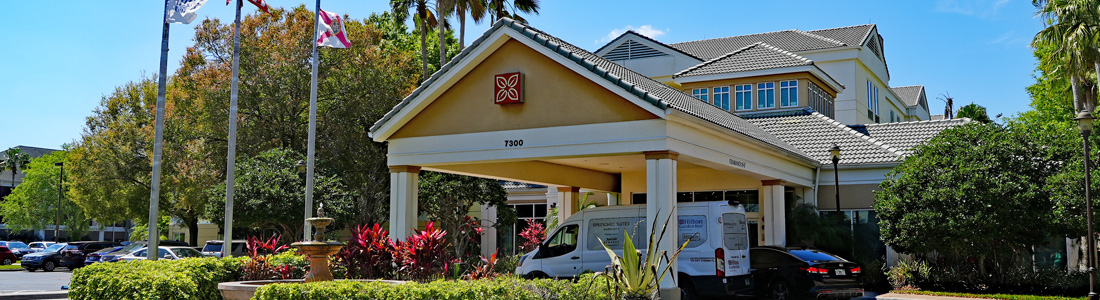 Exterior view of the front entrance to Hilton Garden Inn Orlando Airport hotel with a shuttle to Port Canaveral