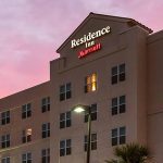 Exterior view of the Residence Inn by Marriott at sunset, featuring a multi-story building with illuminated windows and signage, under a pink and purple sky.