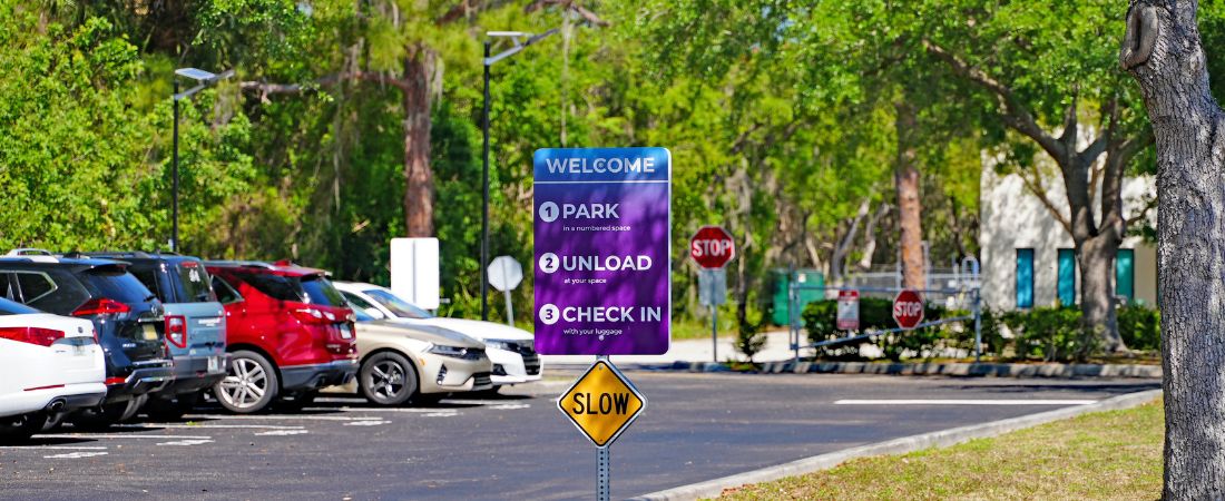 sign at Go Port Plaza with free cruise parking instructions that reads "park, unload, check in" with cameras and gate in background