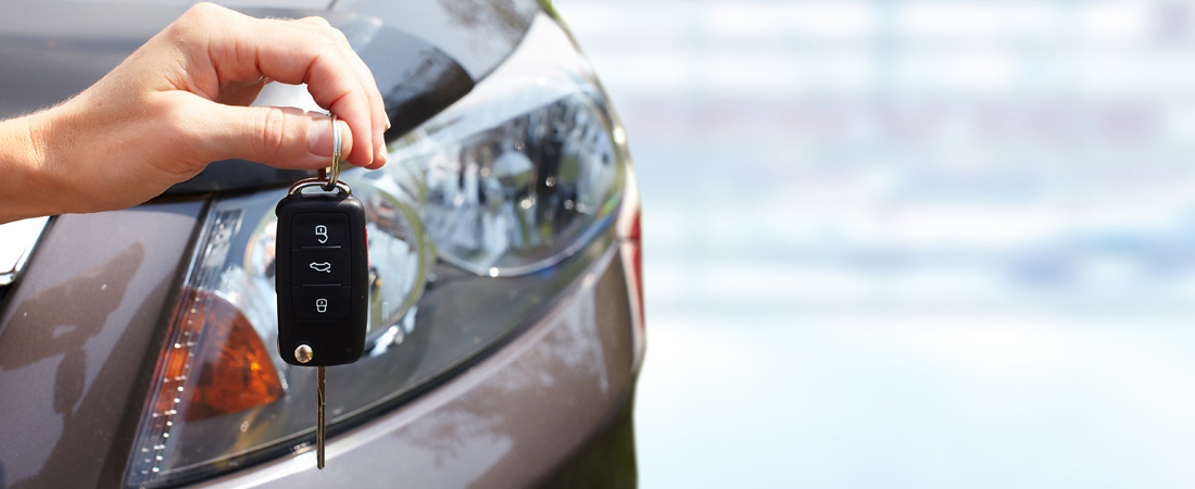 Person's hand holding a key to the grey rental car in the background