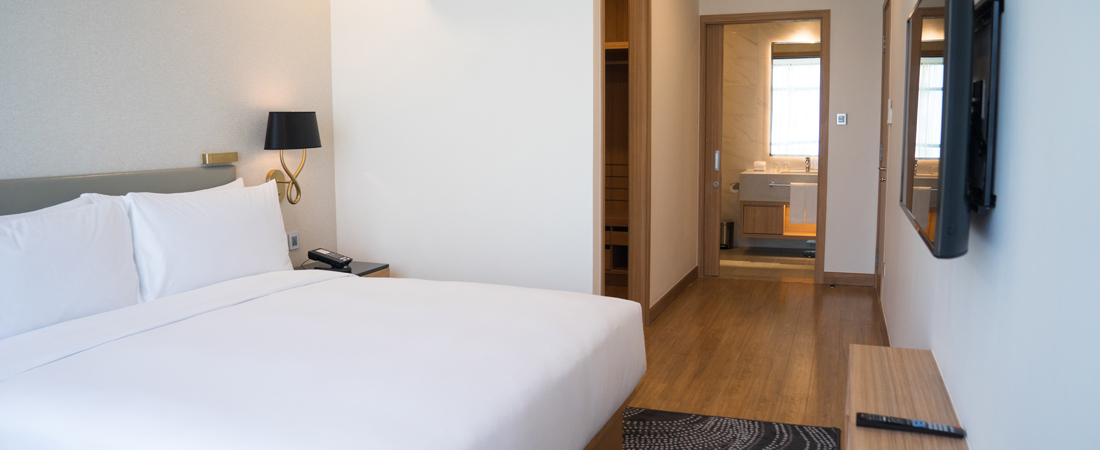 Modern room with in a hotel near the airport that has one king bed with white sheets, white walls, hard wood flooring, flat-screen, and walk way to the bathroom
