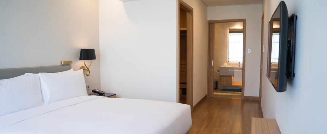Room in a hotel near the Orlando Airport with a bed with white sheets, television on the wall and a hallway leading to a bathroom