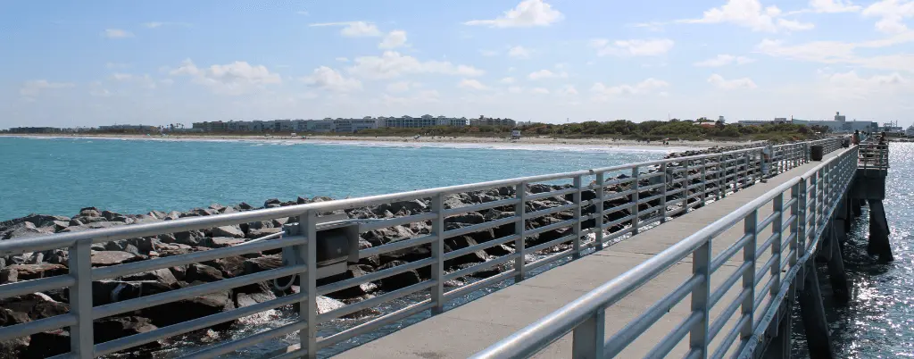 Long fishing pier extending over rocky jetties into bright turquoise water at Jetty Park in Port Canaveral.