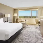 hotel room near port canaveral with large king bed covered in white sheets with television and dresser on the right and desk in front of window showing blue sky