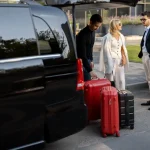 Cruisers standing next to large red and black suitcases as driver loads luggage into black car for private transportation service