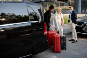 Cruisers standing next to large red and black suitcases as driver loads luggage into black car for private transportation service
