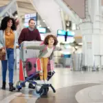 child riding luggage cart pushed by parents before international flight to florida