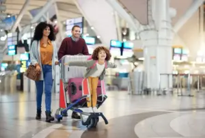 child riding luggage cart pushed by parents before international flight to florida