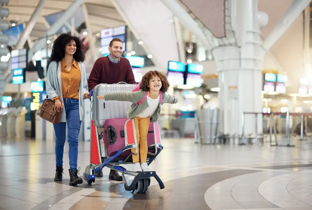 child riding luggage cart pushed by parents before international flight to florida