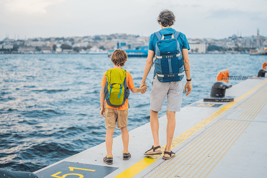 Father and son stand hand in hand, about to embark on their cruise on the dock.