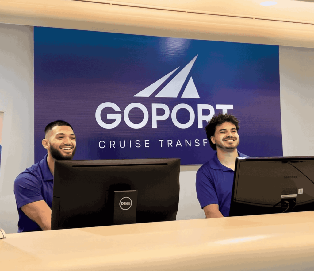 Two go port employees stand shoulder to shoulder, smiling, while behind the go port desk located at MCO