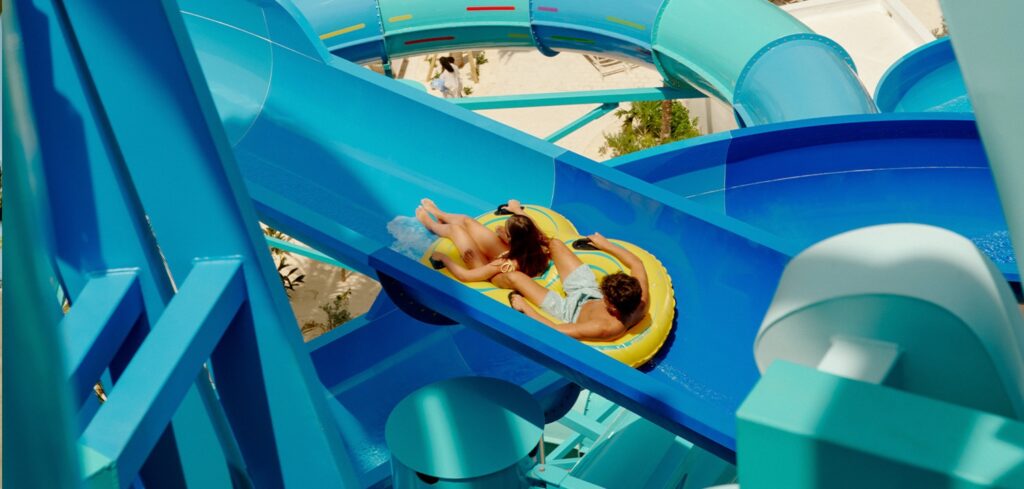 Two guests ride a yellow inner tube down a winding blue waterslide at Great Tides Waterpark.